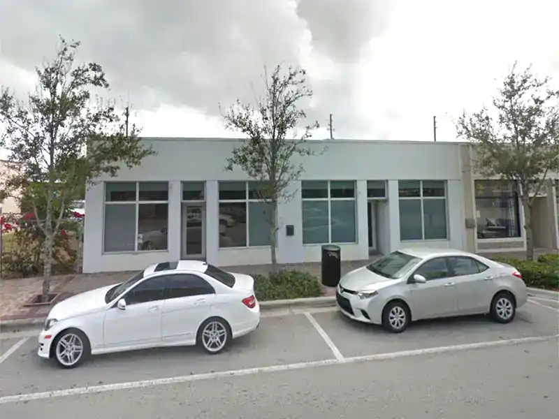 Building facade with large windows and two parked cars.