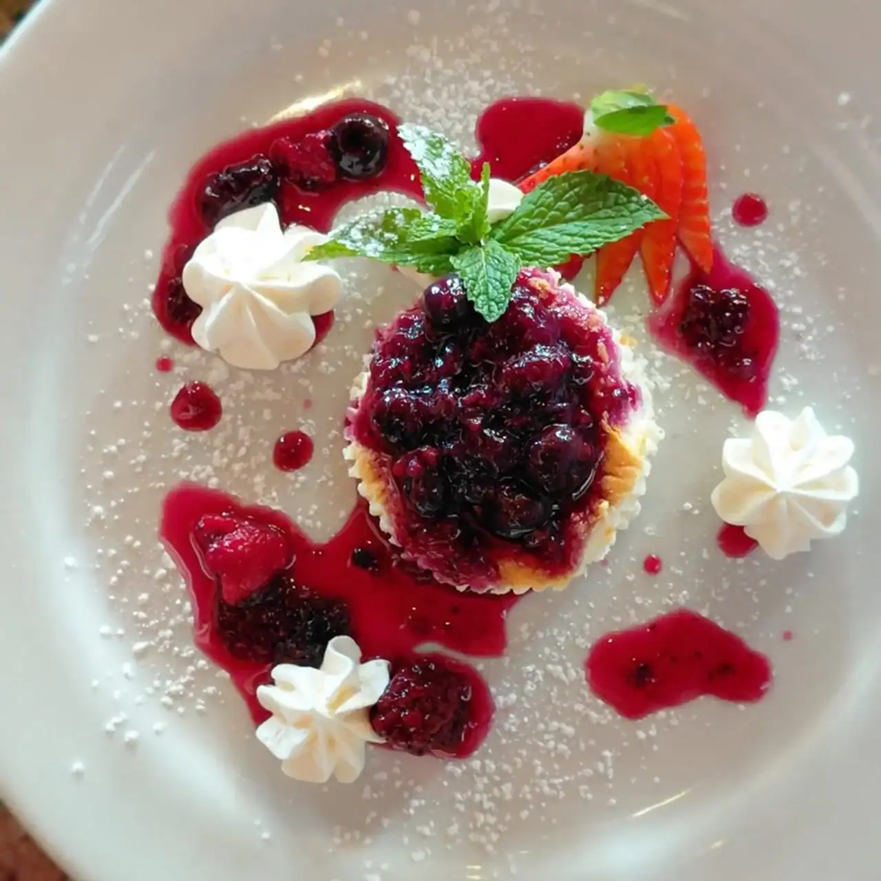 Cherry dessert with berries, mint, and whipped cream on a white plate.