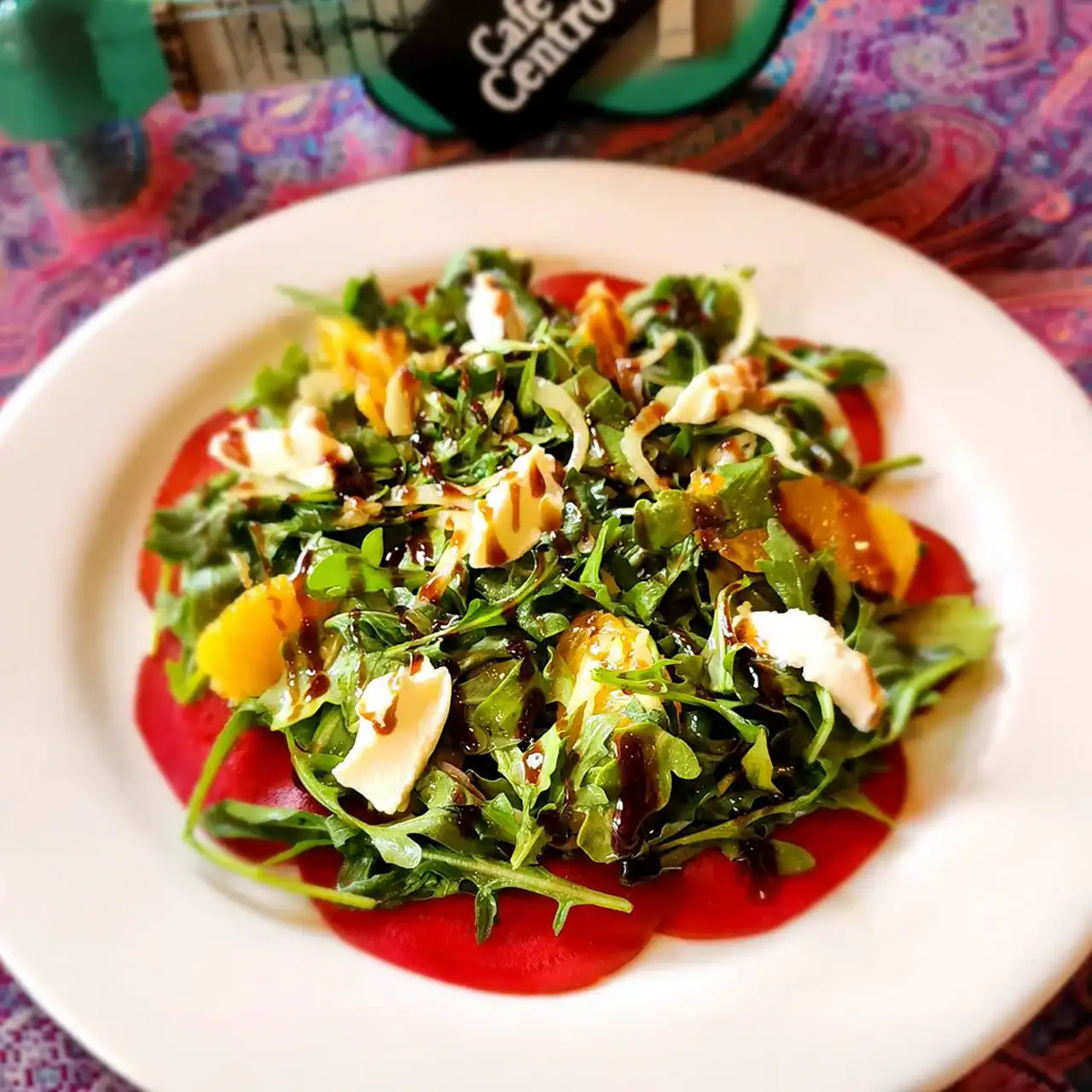 Arugula salad with peaches, cheese, and balsamic glaze on a white dish.