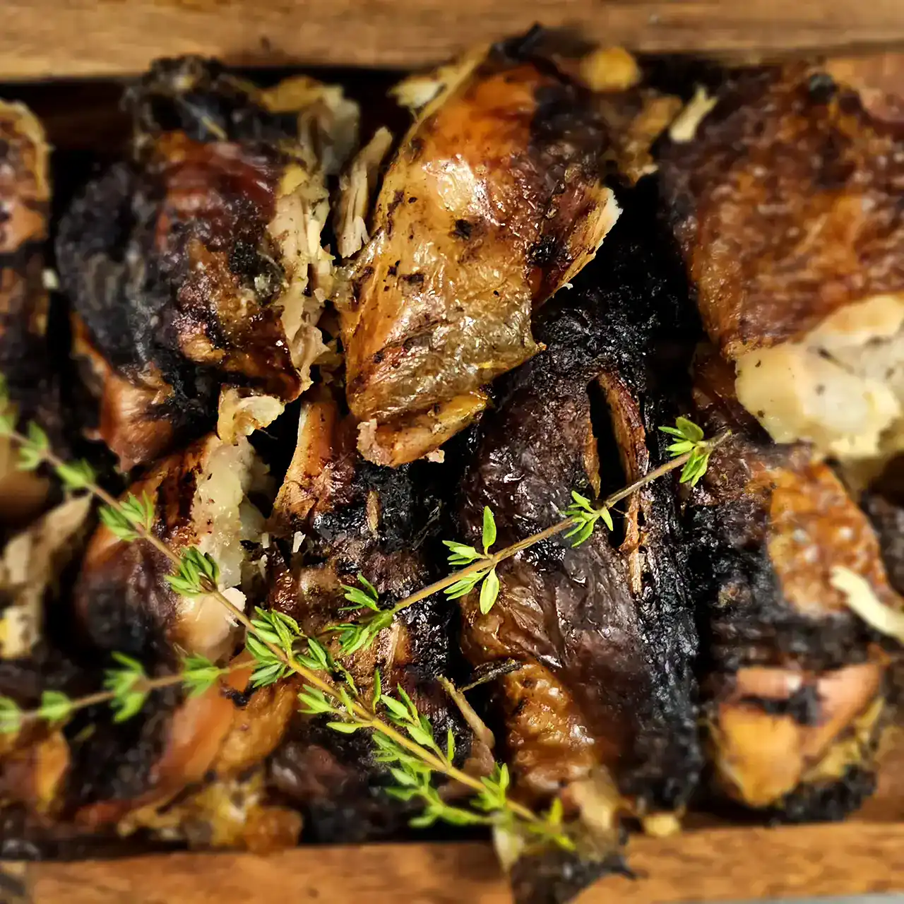 Grilled chicken pieces garnished with fresh thyme on a rustic wooden surface.