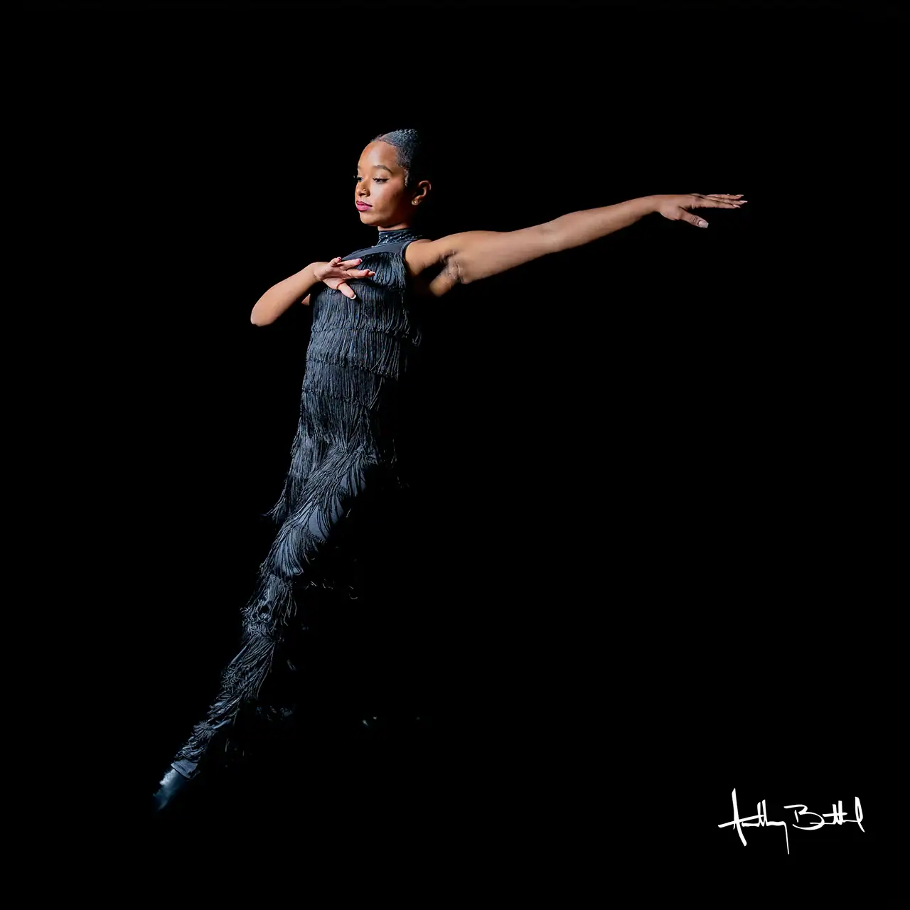 Ballet dancer in black costume executing a graceful pose against a dark background.
