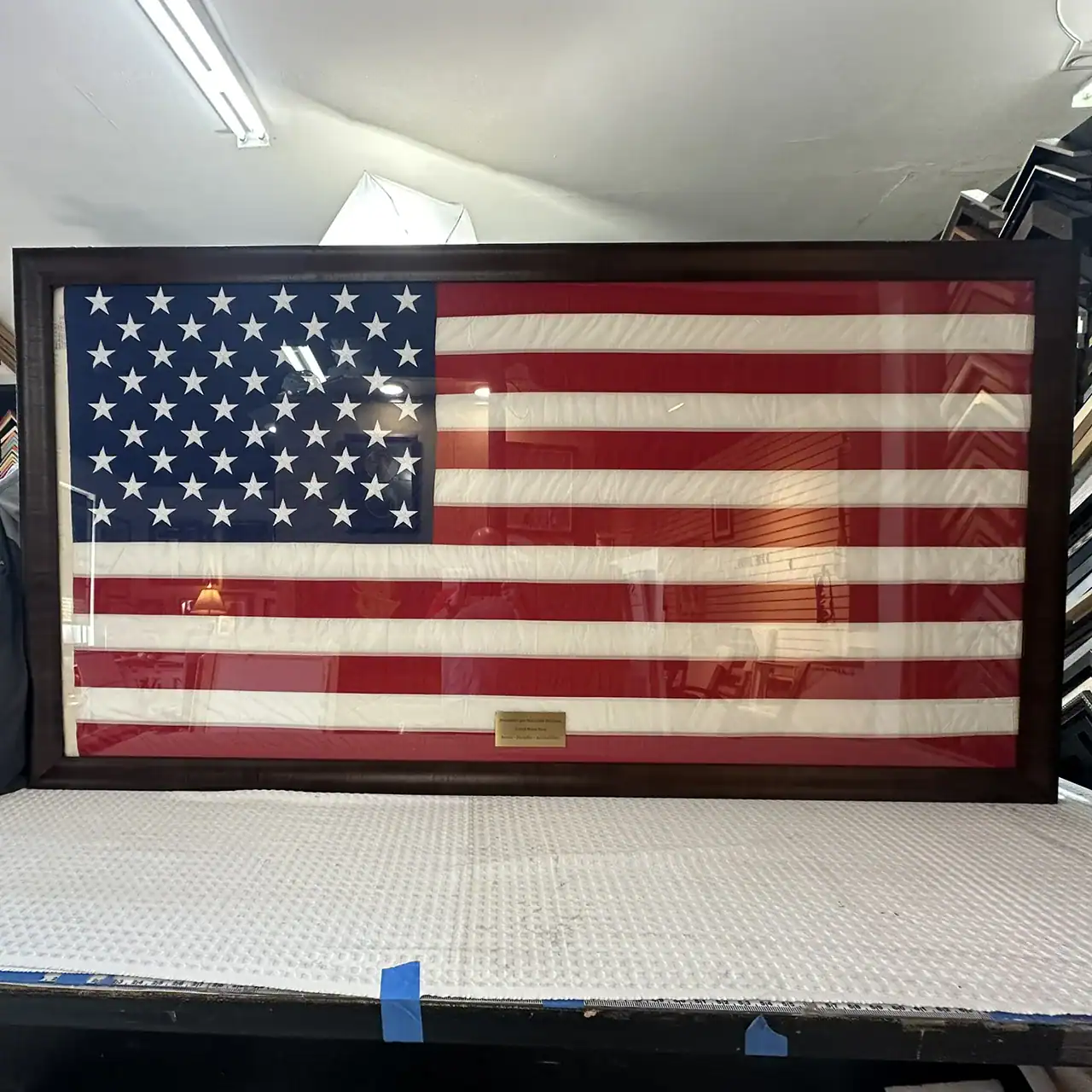 American flag framed display, hanging on a wall with a plaque at the bottom.