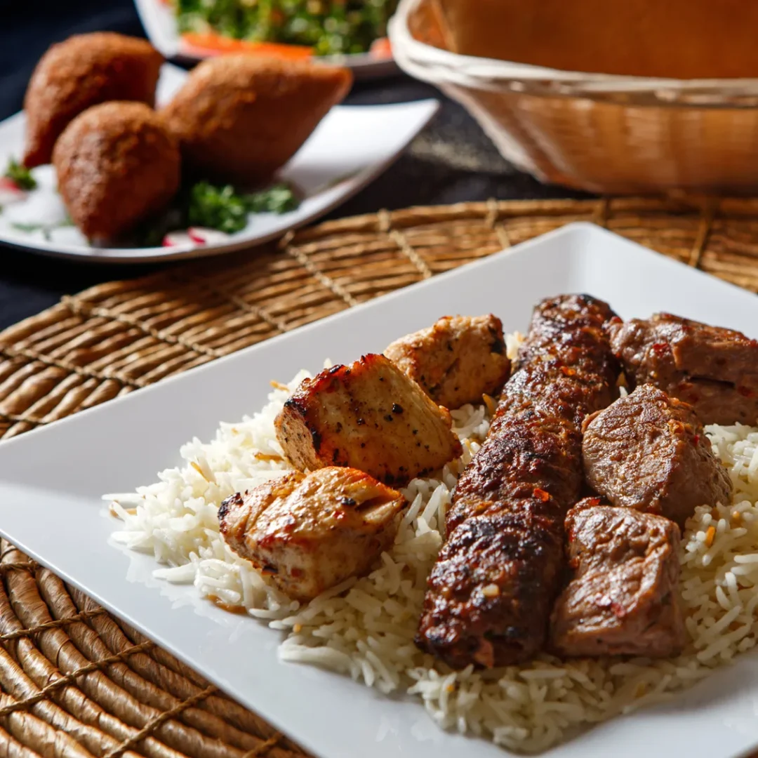 Grilled meat served over white rice with roasted potatoes and a side salad in the background.