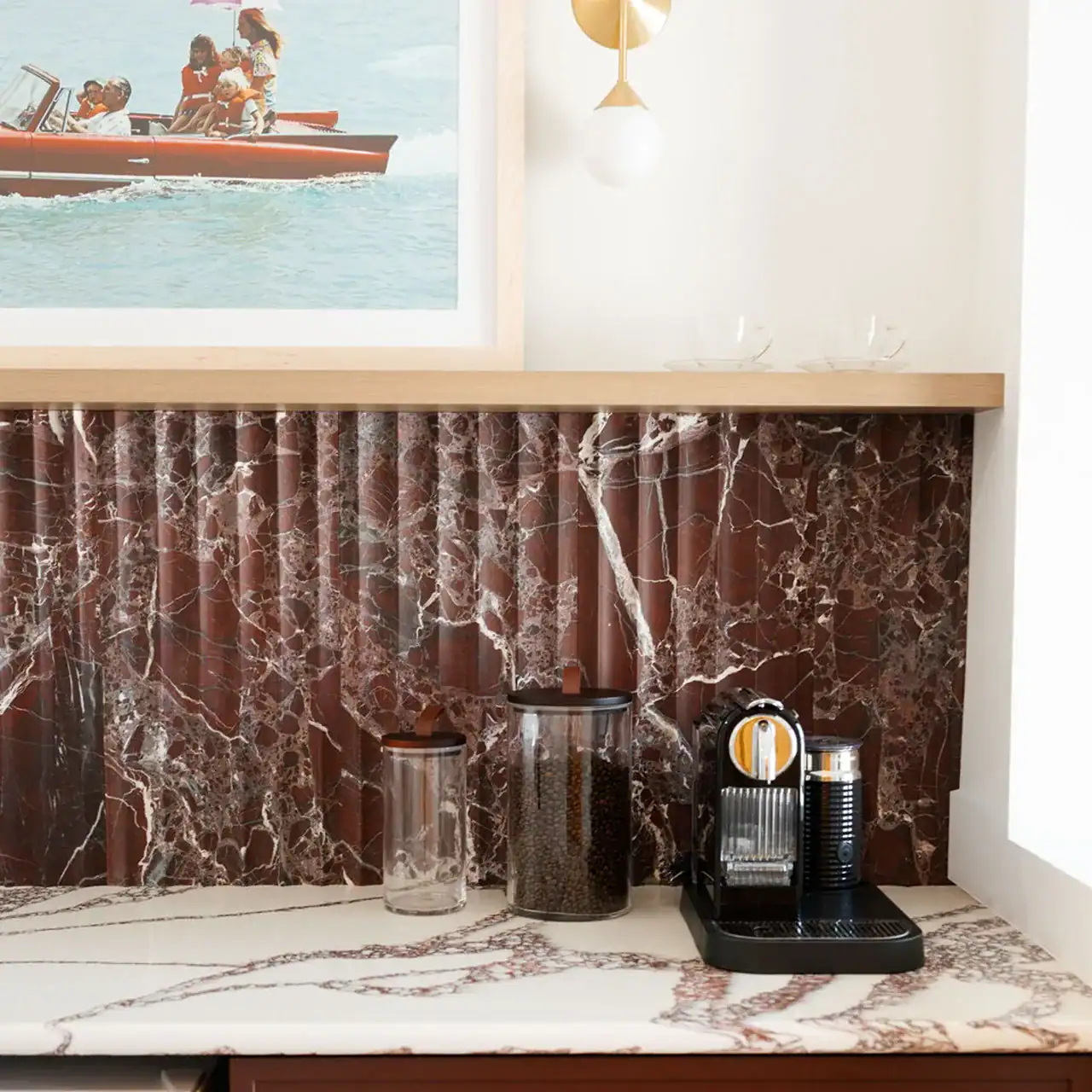 Coffee station with a marble countertop, coffee machine, and jars against a red marble backsplash.