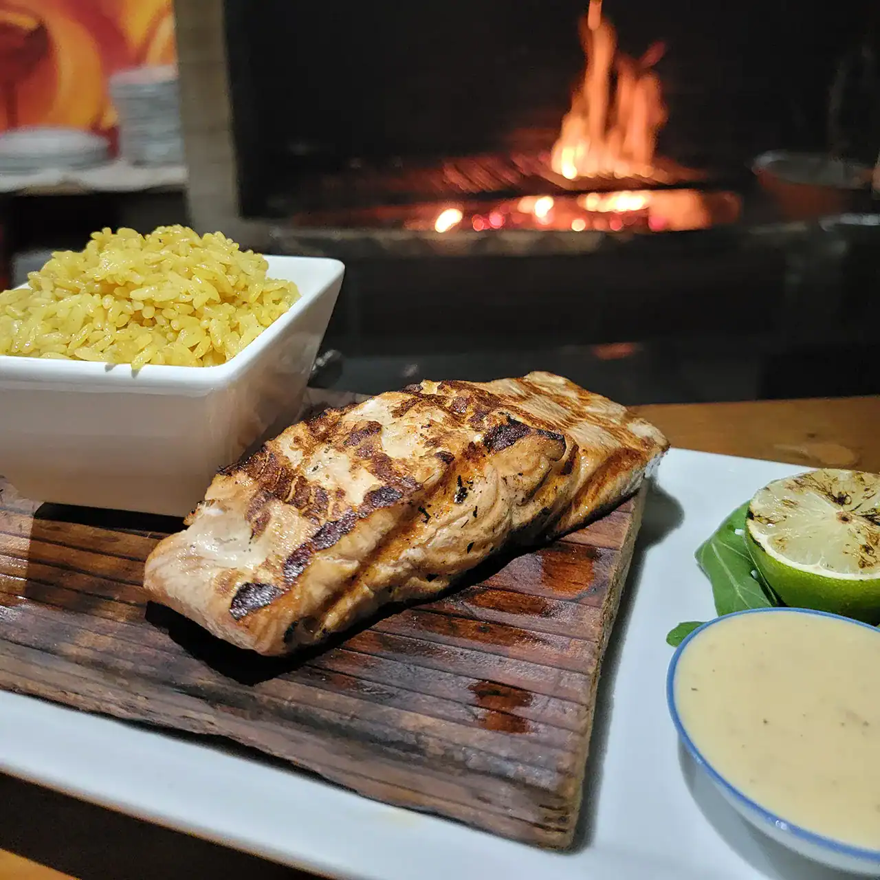 Grilled fish fillet served with yellow rice, lime wedge, and creamy sauce on a white plate.