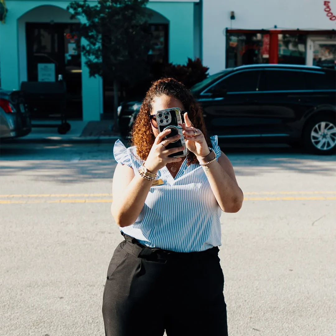 Woman holding a smartphone, taking a picture outdoors.