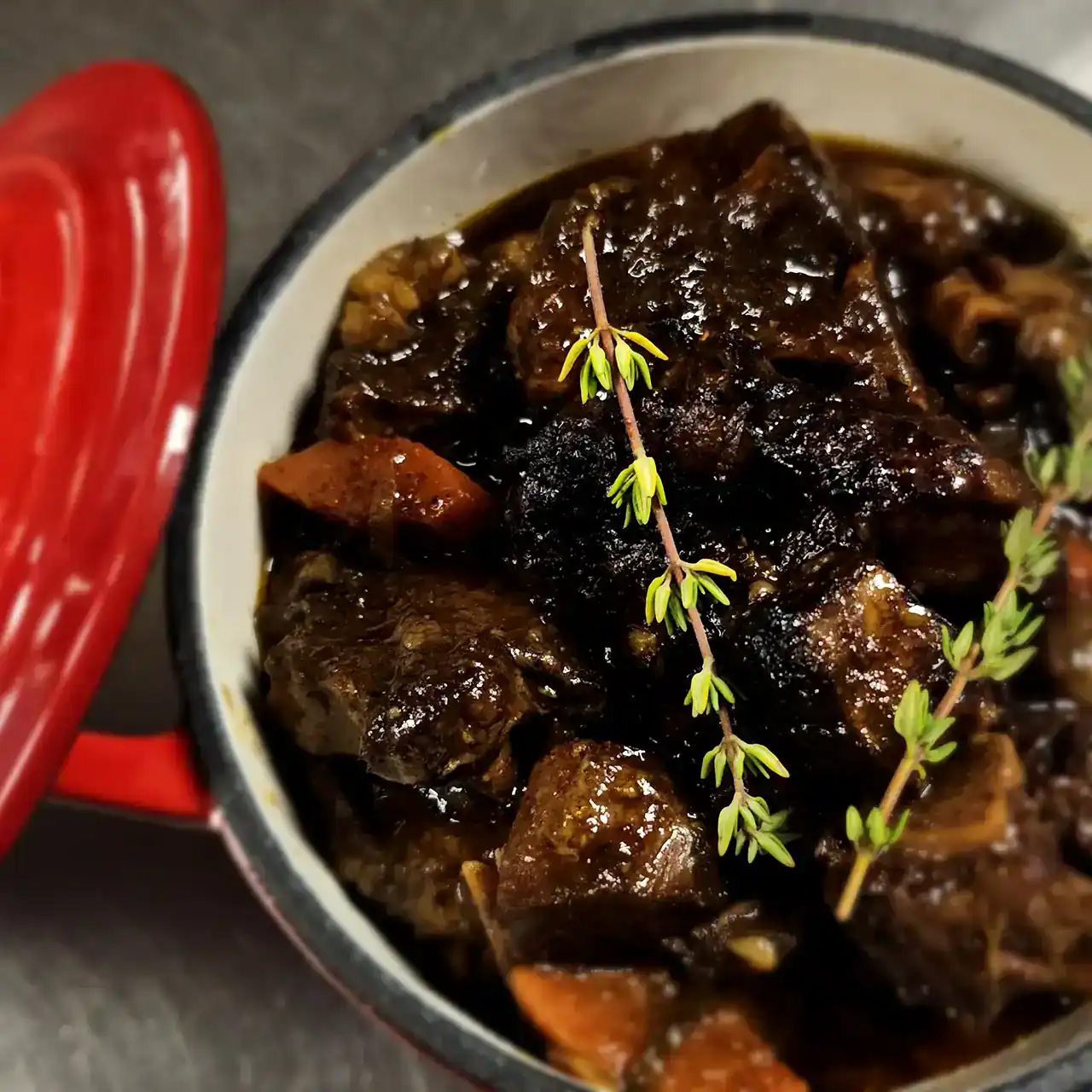 Beef stew with herbs and vegetables in a bowl, garnished with thyme sprigs.