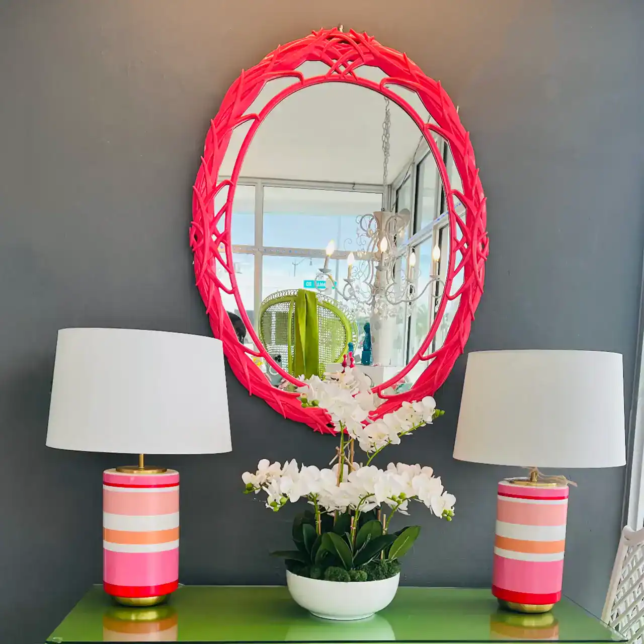 Pink oval mirror with woven frame hanging on a gray wall.
